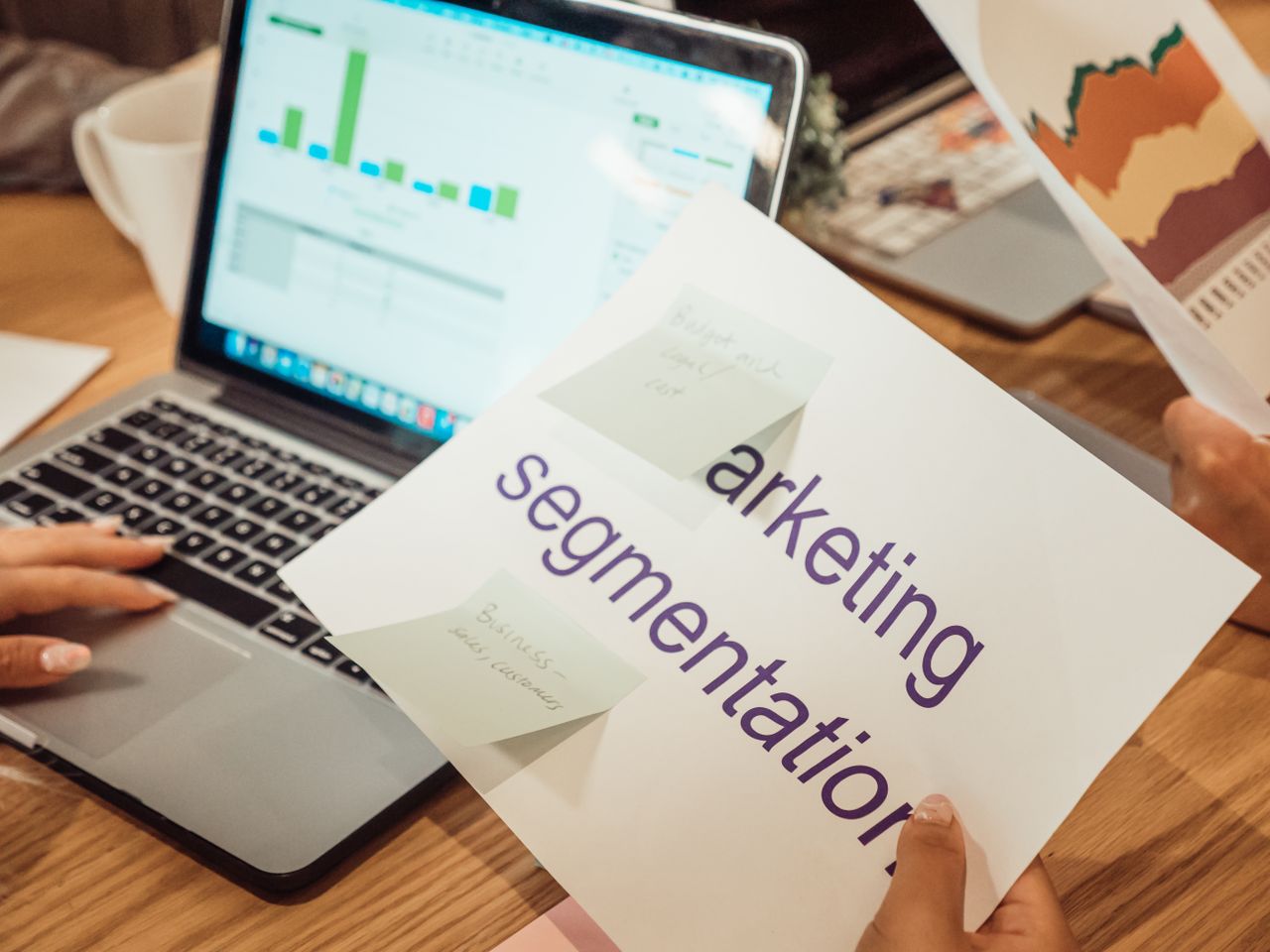 Un espace de travail contemporain où des mains analysent des données marketing sur un ordinateur portable et des documents papier.